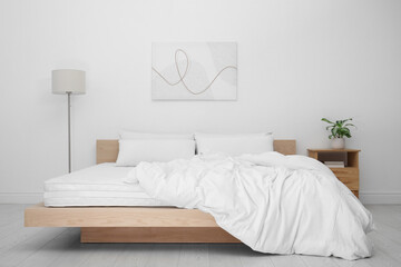 Wooden bed with soft white mattress, blanket and pillows in cozy room interior