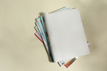 Stack of magazines and one open with blank page on beige background, top view