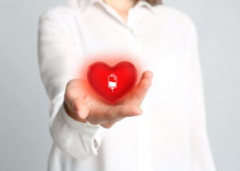 Woman holding red heart in hand on light grey background, closeup. Blood donation concept
