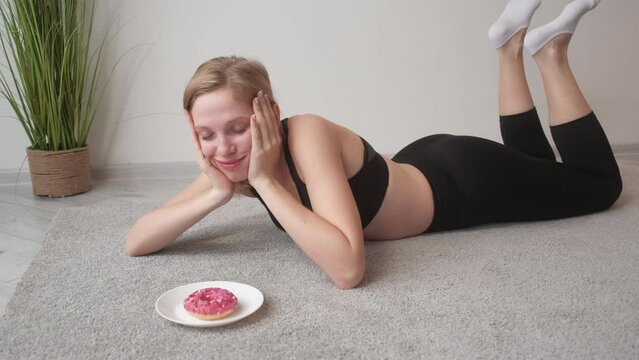 Dessert lover. Healthy diet. Figure care motivation. Inspired hungry athletic woman in activewear enjoying looking at delicious sweet doughnut lying on floor.