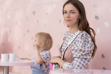 cheerful young woman and her 4-year-old daughter eating ice cream sitting at table in cafe