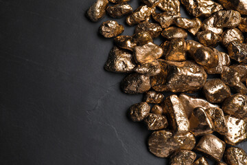 Pile of gold nuggets on black table, flat lay. Space for text