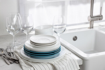 Different clean dishware, cutlery and glasses on countertop near sink in kitchen