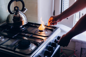 A man's hand with a match lights a gas burner or a gas stove in the kitchen