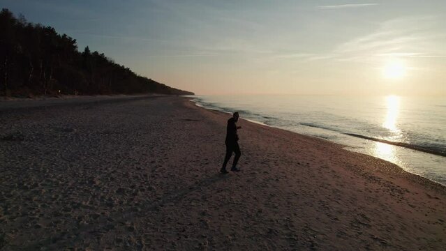 The guy in the tracksuit runs across the beach, the sun going down in the background.