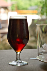 Glass of dark amber beer on the table in outdoors summer restaurant