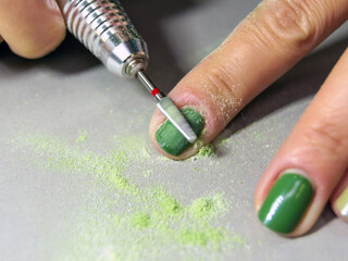 The process of cutting the gel nail polish with the help of a manicure mill. Removal of varnish from women's nails. green manicure Horizontal image.