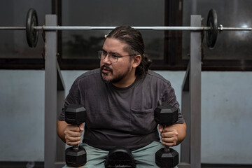 A man in his late 30s at the gym resting in between sets. Contemplating about his next exercise. A...