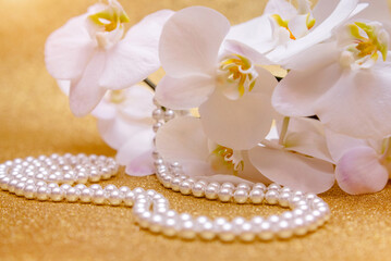 white Orchid and pearl necklace on a shiny gold background