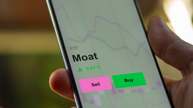 Invest in ETF moat fund on a screen. A phone shows the prices of competitive advantage companies etf