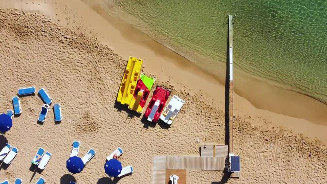 Aerial top down footage view of parasol sun umbrellas, wheel chair handicap access ramp leading from beach to transparent sea on a sunny day in Protaras, Famagusta, Cyprus from above with no people