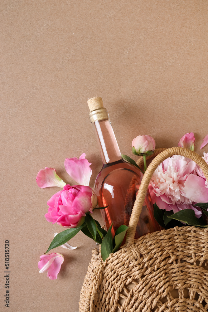 Canvas Prints Wicker bag with bottle of rose wine and beautiful pink peonies on brown background, top view. Space for text