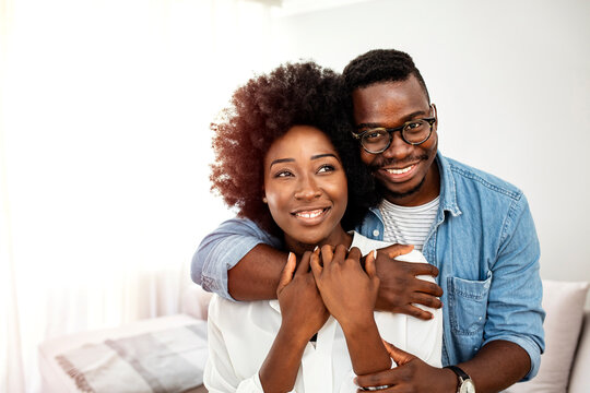 Happy mature black couple bonding to each other and smiling. Portrait of smiling black man embrace his wife from behind and looking at camera. Portrait of a happy young couple