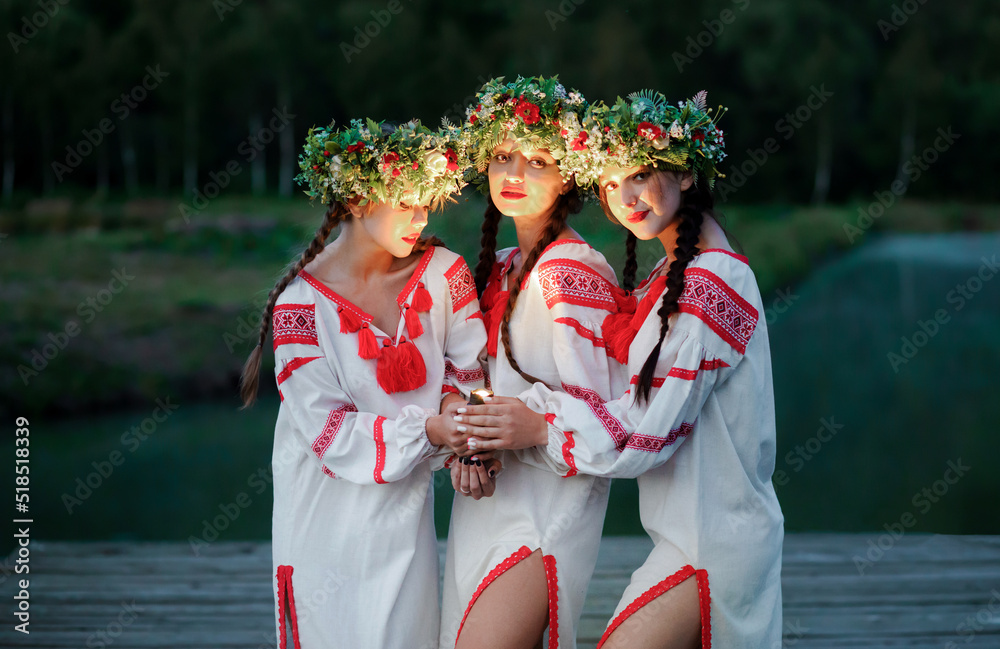 Wall mural Young pagan girls with a lantern in their hands near the lake in the evening. Celebration of summer Kupala