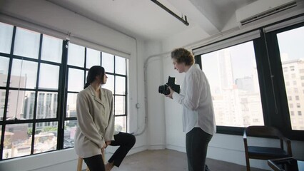Young woman in casual white shirt and blue jeans, professional or hobby photographer using retro vintage film medium format camera, taking portrait picture of beautiful model in photo studio in LA. 