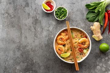 Laksa Shrimp bowl. glass noodle dish, top view, copy space. Asian Malaysian food with shrimps, bok choy, lime, ginger, and chili. Most variations of laksa are prepared with spicy coconut soup.