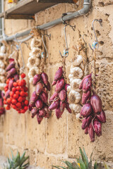 Bunch of  and fresh white garlic, red onion and cherry tomatoes hanging on a stone wall in a street food market, vertical