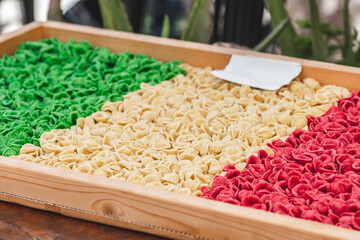 Fresh green, white and red orecchiette or orecchietta pasta drying under the sun on a wooden board, made with durum wheat and water, handmade pasta typical of Puglia, Apulia, Southern Italy, close up