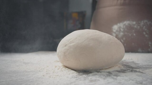 The dough falls on the table. Flour spreads. Close-up.