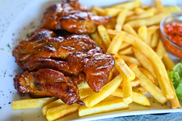 Grilled chicken meat and French fries served on table in restaurant. Smoked chicken meat on plate. Tasty lunch. 