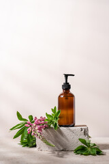 Cosmetic dark glass bottle with dispenser on stone podium with flowers. Beauty and Spa concept