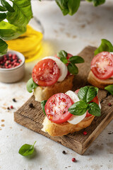 Italian bruschetta with tomatoes, mozzarella on rustic wooden board with basil greens in blur and...