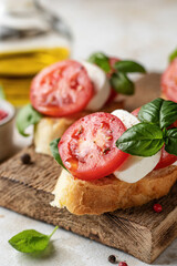 Bruschetta with tomatoes, mozzarella and basil on rustic wooden board close up with ingredients