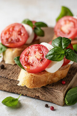 Italian bruschetta with tomatoes, mozzarella and basil on rustic wooden board close up
