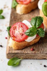 Bruschetta with tomatoes, mozzarella and basil on rustic wooden board close up