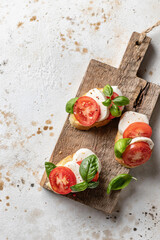Italian bruschetta with tomatoes, mozzarella and basil on rustic wooden board top view, text space