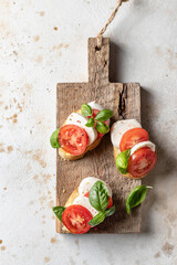 Italian bruschetta with tomatoes, mozzarella and basil on rustic wooden board top view