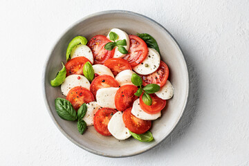 Italian caprese salad with sliced tomatoes, mozzarella, basil, olive oil on white background with copy space. Top view