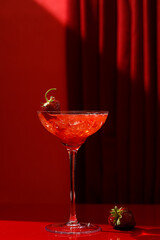 A red cocktail with strawberries in a glass is on the table. A red curtain and a red table.