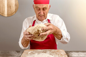 Chef-cooker in chef's hat and apron working in bakery, kneading dough for bread. Senior...