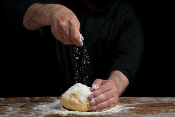 Strong male hands kneading the dough for homemade bread. Baker man kitchener in a black shirt...