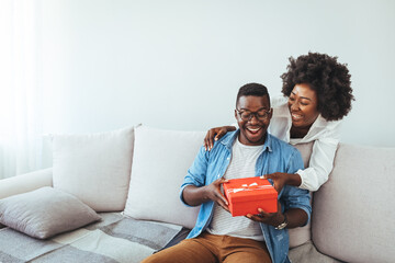 African descent brazilian couple exchanging gifts at home. Surprised woman receiving Birthday...