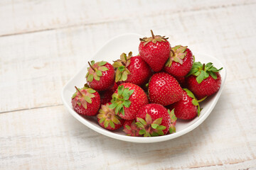 strawberries in a plate on a white wooden background, fresh red berries, concept of fresh fruits and healthy food