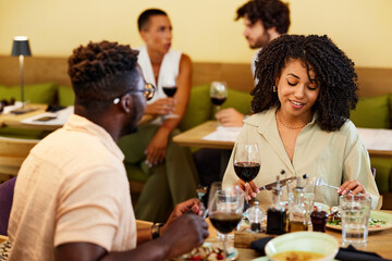 A happy multiracial couple sits in a restaurant, chatting and having dinner together.