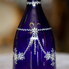 antique glass bottle with glasses of blue color in a luxurious interior. crystal service with white painting. glass close-up