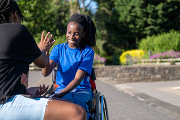 Teenage girl (16-17) in wheelchair with friend playing in park