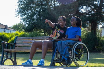 Teenage girl (16-17) in wheelchair with friend relaxing in park - obrazy, fototapety, plakaty