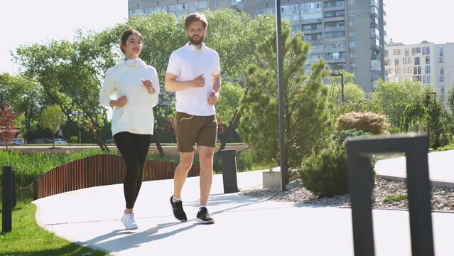 Happy Caucasian young male and female joggers jogging together on sunny summer day in sportswear. Cheerful man and woman running in thee morning. Couple of runners. Fitness concept.