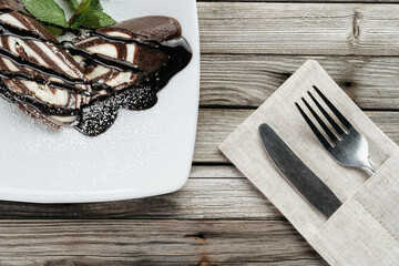 Chocolate swiss roll cake on the white plate, decorated with chocolate topping and mint leaf.