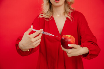 Unrecognizable woman with syringe applying injection to fresh red apple on re isolated background....