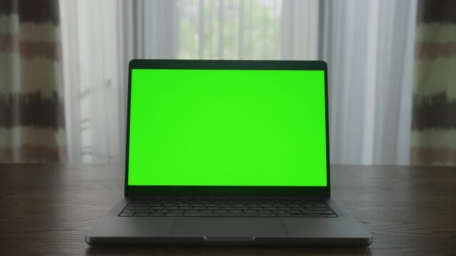 Slow optical zoom in into a laptop computer with green screen chroma key indoors