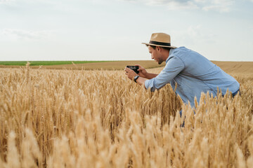 Naklejka na ściany i meble Happy farmer photographing crops with phone while standing in his growing wheat field. 