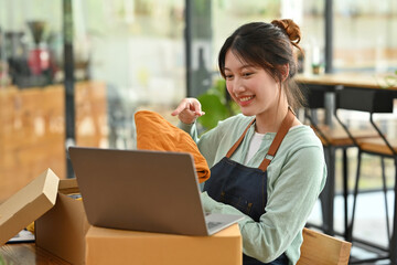 Asia girl SME owner smile work on laptop for live on social media, selling a shirt.
