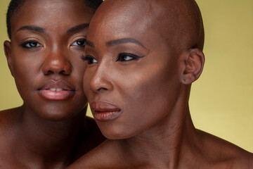 Studio portrait of two women cheek to cheek against yellow background