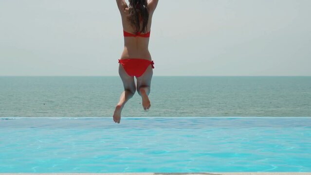 Girl in Bikini Having Fun Running Jump in Infinity Pool with Amazing Sea View on Sunny Day at Beach Villa in Resort Hotel, Slow Motion. Happy Excellent Vacation.