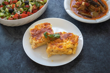 Pasta casserole bechamel sauce topped with melted mozzarella cheese and served in a white baking dish on a table (Turkish name; firinda makarna or firin makarna)